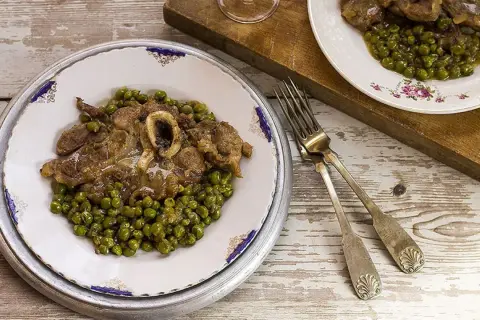 Un piatto di ossobuco con piselli, servito su un tavolo di legno rustico. Le forchette d'argento sono pronte per gustare questa delizia.