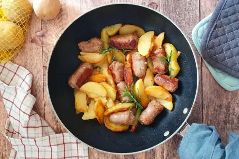 Salsiccia e patate in padella, dorate e profumate, con rametti di rosmarino. Un piatto rustico e invitante.