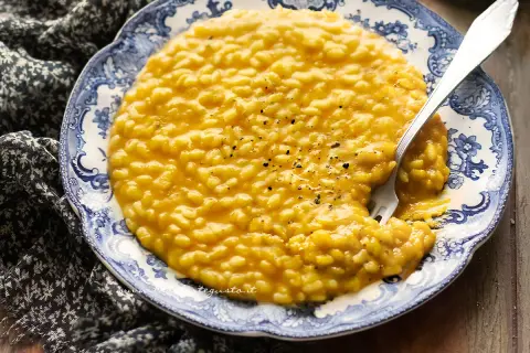 Un invitante risotto con la zucca cremoso, guarnito con pepe nero, su un piatto decorato con un motivo blu e bianco.