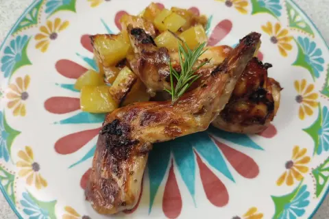 Roasted rabbit pieces with golden potatoes and a rosemary sprig on a colorful floral plate.