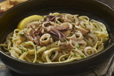 Un piatto invitante di pasta con calamari, guarnito con prezzemolo fresco e una fetta di limone.