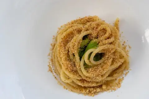 Un piatto di pasta alla carrettiera, spaghetti conditi con mollica tostata e verdure verdi, serviti su un piatto bianco.