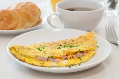 Deliziosa omelette con prosciutto e formaggio filante, guarnita con erba cipollina. Perfetta per una colazione o un brunch.