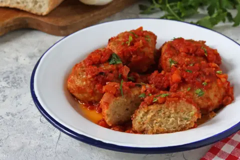 Polpette di pane succulente in salsa di pomodoro, guarnite con prezzemolo fresco. Un piatto casalingo che sa di tradizione.