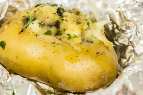 Patate ripiene al forno, dorate e fumanti, avvolte in carta stagnola, con un ripieno cremoso e erbe aromatiche.