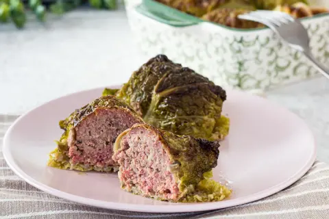Involtini di verza con carne succulenta, uno tagliato a metà per mostrare il ripieno saporito.