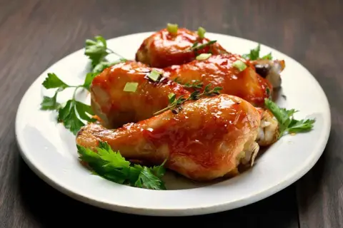 Tre cosce di pollo glassate, guarnite con erbe aromatiche e cipollotto, un delizioso pollo alla birra pronto da gustare.