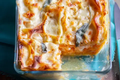 Lasagne con zucca dorate e filanti, guarnite con foglie di salvia, in una teglia di vetro.