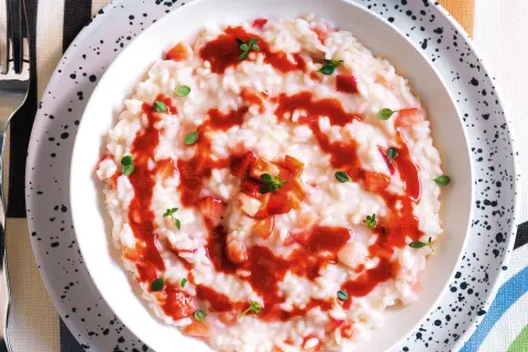 Un cremoso risotto alle fragole, guarnito con salsa di fragole e foglioline verdi.