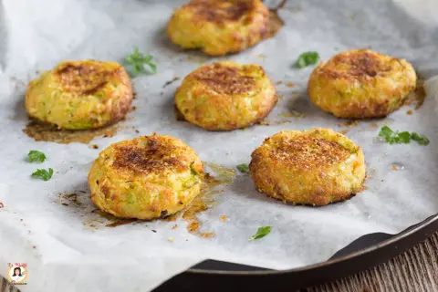 Sei polpette di zucchine dorate e croccanti, appena sfornate, su carta da forno.