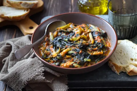 Cicoria in padella, un piatto rustico e saporito, servito in una ciotola con pane fresco e un bicchiere d'acqua.