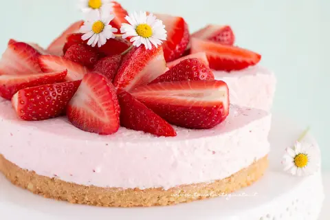 Delizioso cheesecake alle fragole, decorato con fragole fresche e fiorellini bianchi.