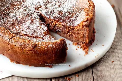 Una deliziosa torta al cioccolato al latte, cosparsa di zucchero a velo, con una fetta mancante che invita ad assaggiarla.