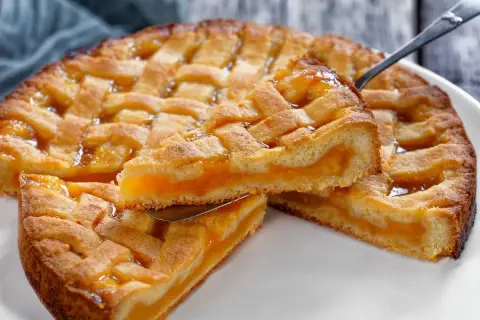Deliziosa crostata senza glutine con ripieno di albicocche, una fetta sollevata da una paletta.