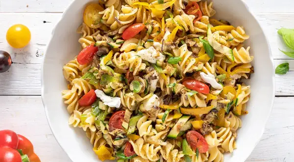 Insalata di pasta con fusilli, pomodorini, zucchine, peperoni gialli e mozzarella fresca. Un piatto colorato e gustoso.