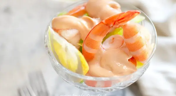 Un delizioso cocktail di gamberi servito in una coppa di vetro, con gamberi succulenti, salsa rosa e una fetta di limone.