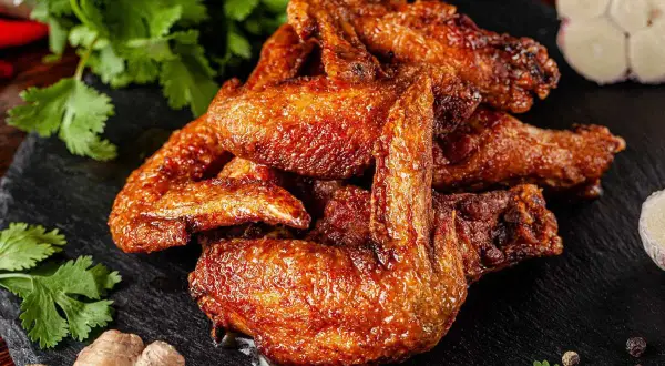 Alette di pollo al forno dorate e succulente, servite su una pietra scura con coriandolo fresco, zenzero e aglio.