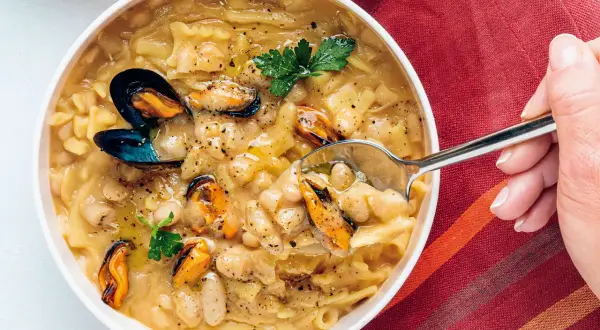 Un cucchiaio raccoglie una porzione di pasta fagioli e cozze, un piatto ricco e saporito, guarnito con prezzemolo fresco.