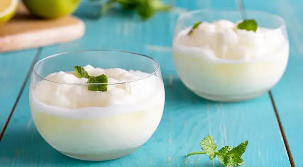 Due bicchieri di sorbetto al limone cremoso, guarniti con menta fresca, su un tavolo di legno blu.
