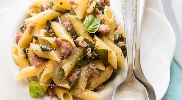 Penne con zucchine e salsiccia, un piatto gustoso e facile da preparare, guarnito con basilico fresco e parmigiano.