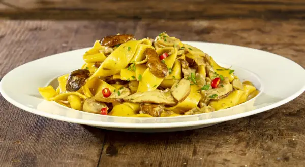 Un piatto invitante di tagliatelle ai funghi porcini, guarnite con peperoncino e prezzemolo fresco, su un tavolo di legno rustico.