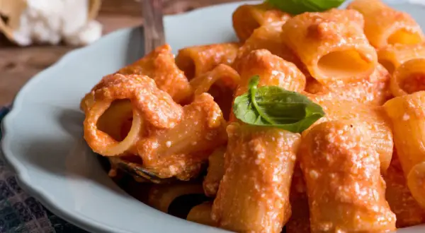Piatto di pasta con sugo cremoso di ricotta e pomodorini, guarnito con basilico fresco.