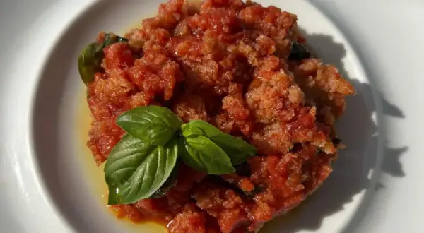 Piatto di pappa al pomodoro, un classico toscano, guarnito con foglie di basilico fresco.