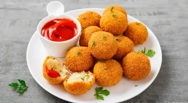 Deliziose polpette di riso dorate e croccanti, servite con salsa di pomodoro e prezzemolo fresco.