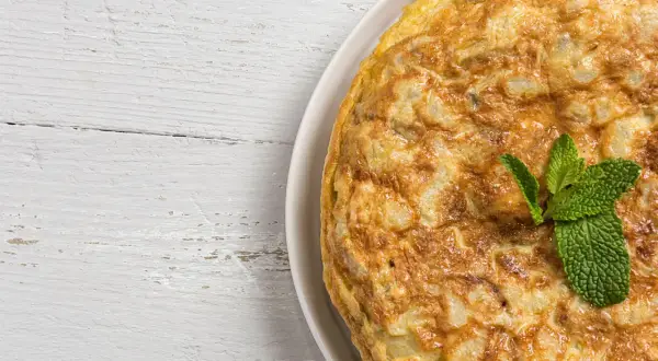 Frittata di cipolle dorata e soffice, guarnita con menta fresca, su un tavolo di legno bianco.