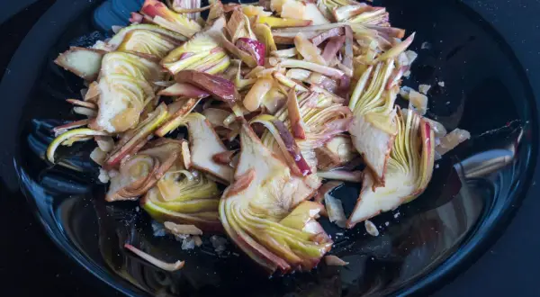 Un piatto nero lucido pieno di un'appetitosa insalata di carciofi crudi, tagliati finemente e conditi.