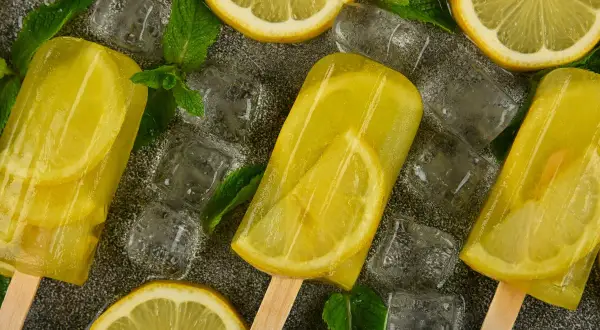Ghiaccioli al limone con fette di limone e foglie di menta, circondati da cubetti di ghiaccio. Rinfrescante e gustoso.
