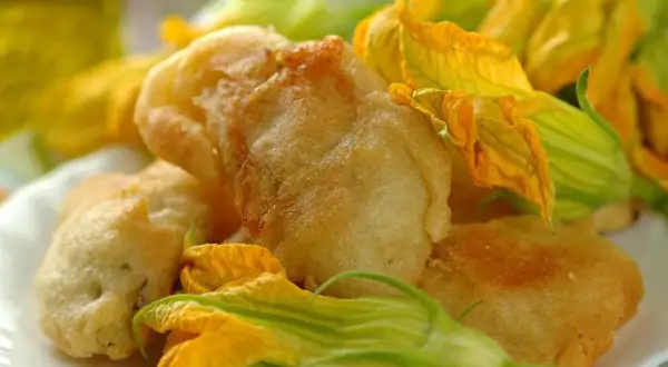 Fiori di zucca in pastella dorati e croccanti, guarniti con i loro stessi fiori freschi.