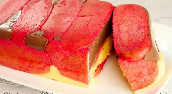 Una fetta di zuppa inglese tradizionale, con savoiardi rossi, crema al cioccolato e crema gialla.