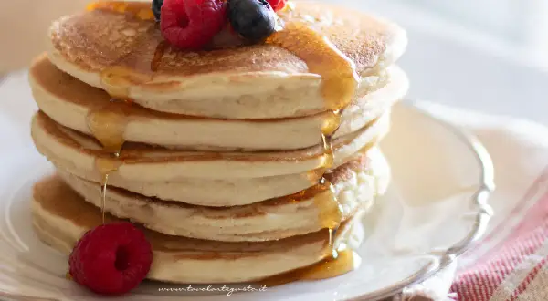 Pancakes senza uova soffici e dorati, inzuppati di sciroppo d'acero e guarniti con frutti di bosco freschi.