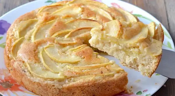 Una fetta di torta di mele senza uova, con mele a fette disposte a spirale sulla superficie dorata.