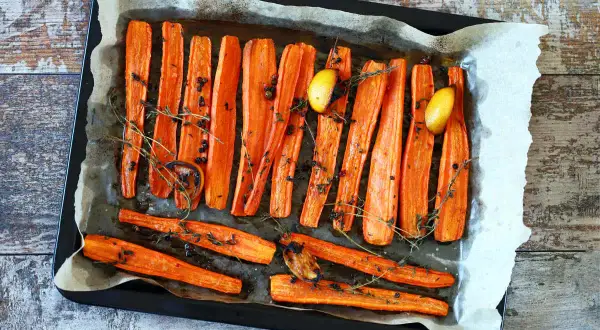 Carote al forno dorate e caramellate, condite con timo fresco, pepe nero e spicchi d'aglio arrostiti, pronte per essere gustate.