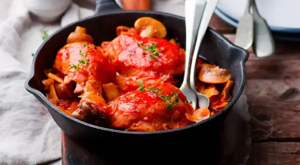 Pollo alla Marengo succulento in padella con funghi e pomodoro, guarnito con timo fresco.