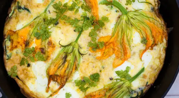 Frittata dorata con fiori di zucca e prezzemolo fresco, un piatto primaverile invitante.