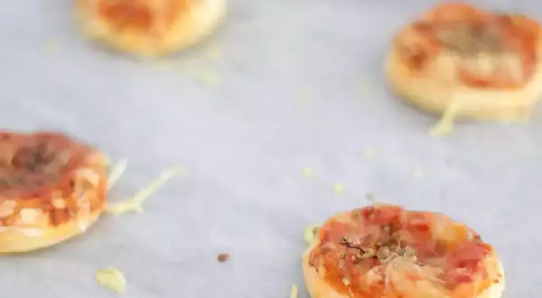 Quattro pizzette di pasta sfoglia appena sfornate, dorate e filanti, pronte per essere gustate.