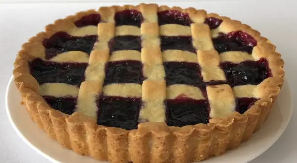 Una crostata di marmellata con una griglia di pasta dorata e un ripieno scuro e invitante.