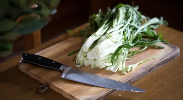 Un coltello affilato pronto a preparare le puntarelle alla romana su un tagliere di legno.