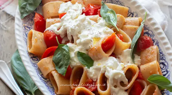 Piatto di pasta con pomodorini e burrata cremosa, guarnito con basilico fresco. Un'esplosione di sapori mediterranei.