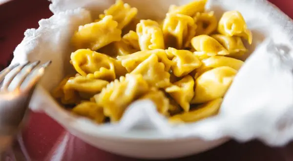 Un primo piatto invitante di ravioli del plin, piccoli e dorati, serviti in una ciotola bordata di bianco.