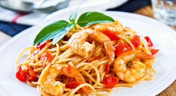 Un piatto invitante di spaghetti con gamberi succulenti e pomodorini freschi, guarnito con basilico.