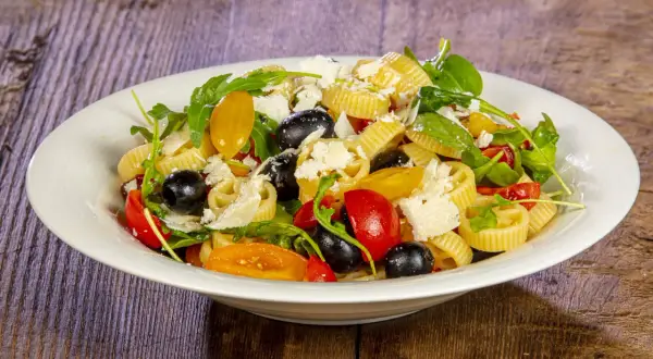 Pasta alla crudaiola con pomodorini, olive nere, rucola e scaglie di parmigiano. Fresca e colorata, un piatto estivo perfetto.