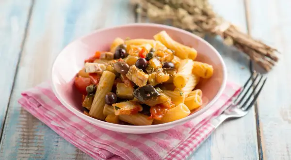 Piatto di pasta con melanzane, tonno, pomodorini e olive nere, condito con erbe aromatiche.