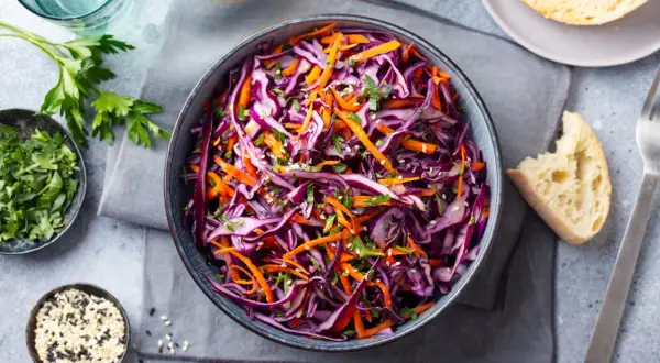 Una fresca insalata di cavolo rosso e carote, guarnita con erbe aromatiche e semi di sesamo, pronta per essere gustata.