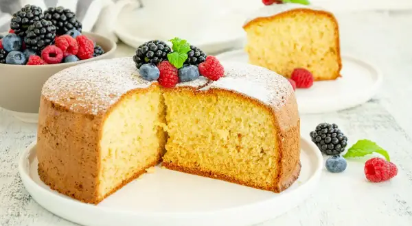 Una soffice torta senza zucchero, spolverata di zucchero a velo e decorata con frutti di bosco freschi, perfetta per una colazione leggera.