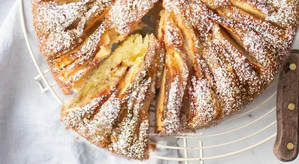 Deliziosa torta di mele in friggitrice ad aria, cosparsa di zucchero a velo, con una fetta tagliata che rivela il morbido interno.