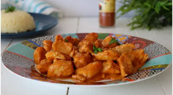 Succulento pollo alla paprika in una salsa cremosa, servito su un piatto colorato con riso bianco sullo sfondo.